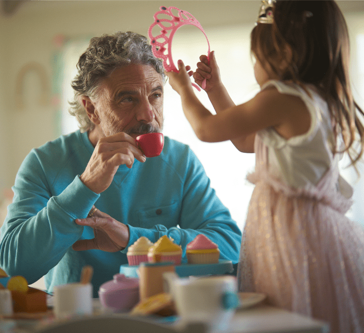 Man sipping from a teacup and girl placing a tiara on his head.