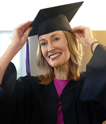 A woman smiling as she graduates in a black cap and gown.