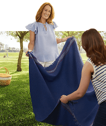 Two women spread a blue blanket on the grass for a picnic in a park.