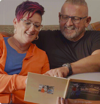 Kimberly, care partner of Michael, and Michael, a real EPKINLY patient, sitting together and reading a book.
